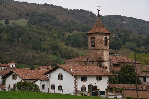 The San Pedro church in Erratzu, Spain surrounded by white houses with red roofs and green hills with trees in the background