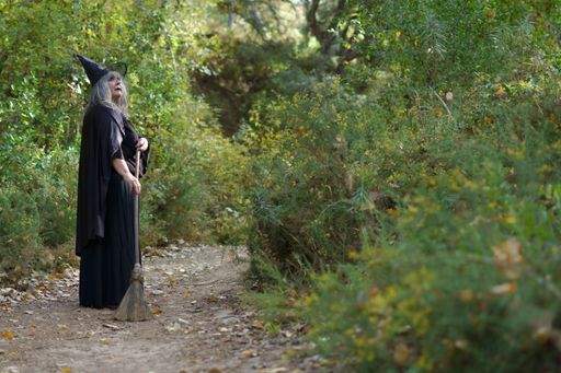 white-haired witch and hat with her broom on a forest trail