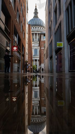 A vertical shot of an alley with the Saint Paul cathedral reflected in a water puddle in London
