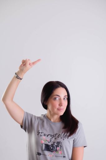 A vertical closeup of a young woman holding her index finger above the head and pointing at something.