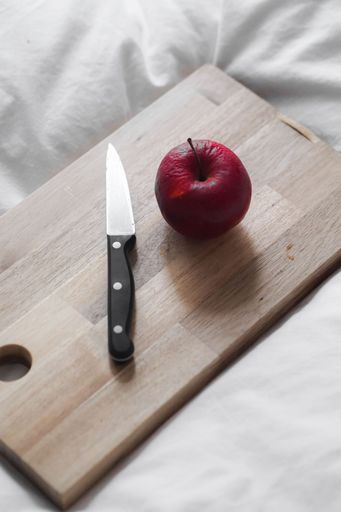 A vertical shot of a wrinkled apple and a knife on a board on white sheets