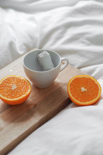 A vertical shot of a sliced orange and an empty white cup with tea bag on a wooden board on white sheets