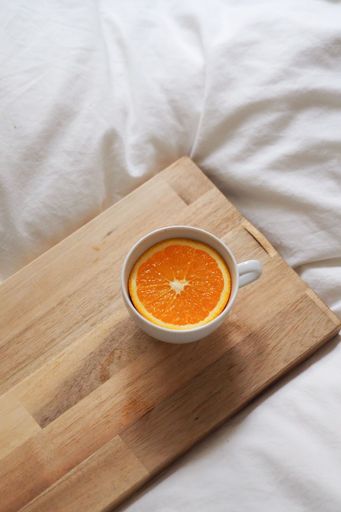 A vertical shot of a cup of tea with an orange slice in it on a wooden board on white fabric