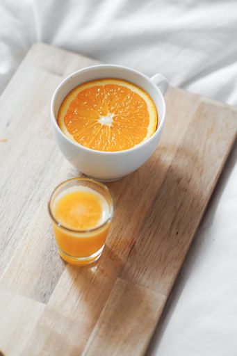 A vertical shot of a teacup with orange slice in it next to a glass of orange juice on a wooden board