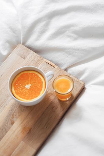 A white cup with an orange slice inside and fresh juice on a wooden board