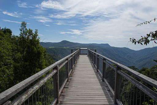 A breathtaking view of a wooden path over the beautiful tree covered mountains under the cloudy sky