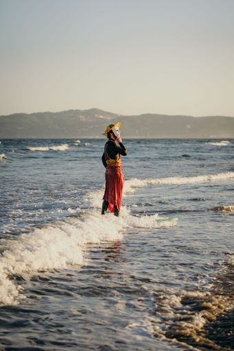 A vertical shot of a person wearing a mask standing in the water on the shore of a beach