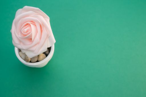 A high angle shot of a vase with small rocks and an artificial rose
