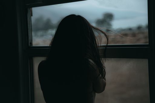 A closeup shot of a female with long hair looking out of the window in a dark room