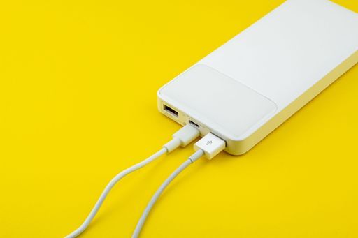 A white power bank with a USB cable on a yellow surface