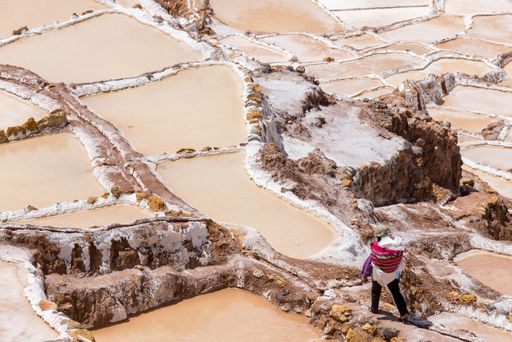 A high angle shot of a man in colorful clothing extracting salt at a mine in Maras, Peru