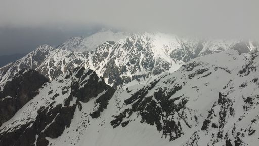 An aerial shot of rocky mountains covered with snow on a cold, gloomy day