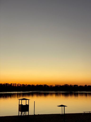 A vertical shot of silhouettes of a watchtower and trees reflecting on a calm lake during dusk