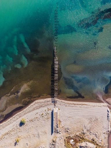 A vertical aerial view of an old abandoned pier at the sandy shore