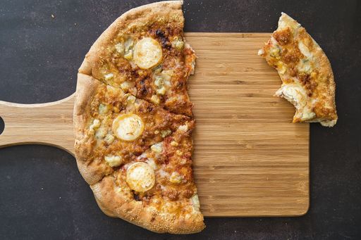 A top view of a tasty half-eaten pizza on a wooden cutting board put on a marble surface