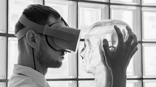A gray scale shot of a person wearing virtual reality goggles holding a transparent mannequin