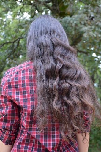 A shallow focus of a female with long dark brown wavy hair wearing a red flanner shirt in a park