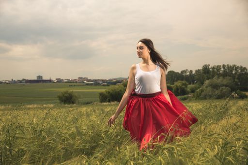 A young girl wearing a red skirt posing in a green wheat field