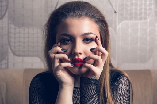 A portrait of a pretty model in a black outfit and red lipstick holding her face by hands