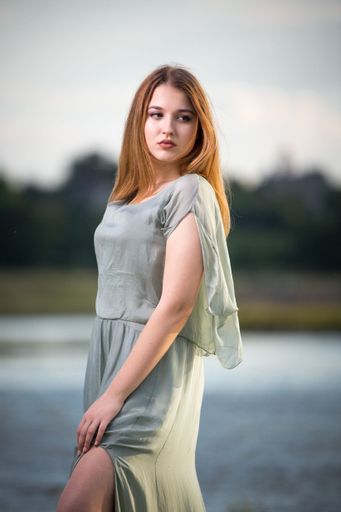 A Vertical  shot of Blonde sexy female in a gray dress standing at seaside at sunset