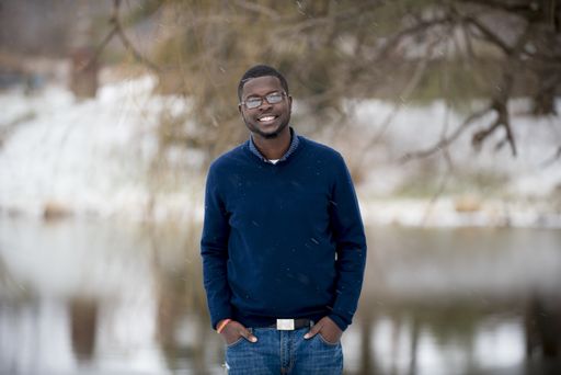 A shallow focus shot of a male standing  with his hands in the pocket while smiling at the camera