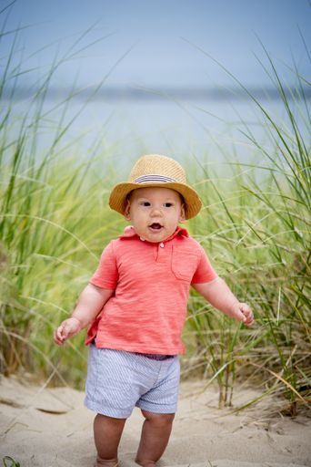 a vertical shot of a cute baby standing on a sandy surface near the beach