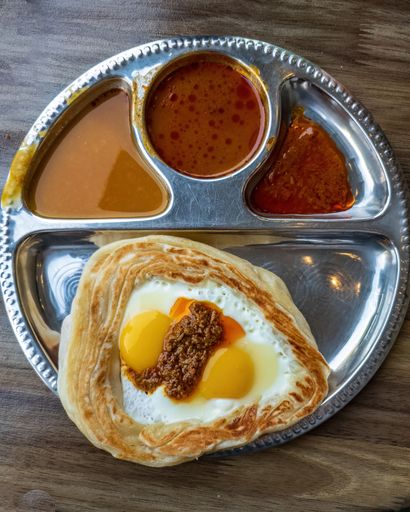 A Roti Sarang Burung served with different gravies, pratha with half cook eggs in the middle and topped with rendang gravy