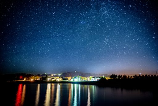 A beautiful shot of buildings with lit lights in the distance near the water under a sky filled with stars