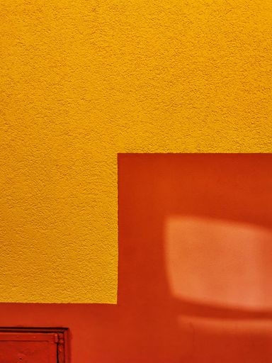 A vertical shot of a cement wall colored in yellow and red with a door visible in the corner