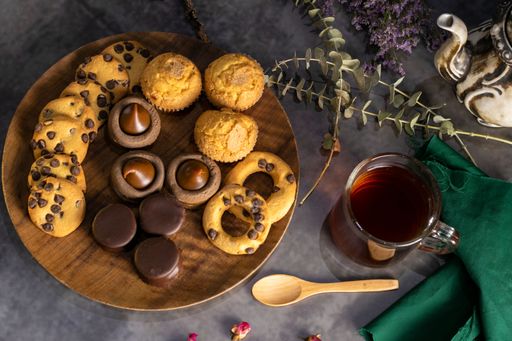 A closeup of delicious cookies on a wooden plate with an old teapot on table