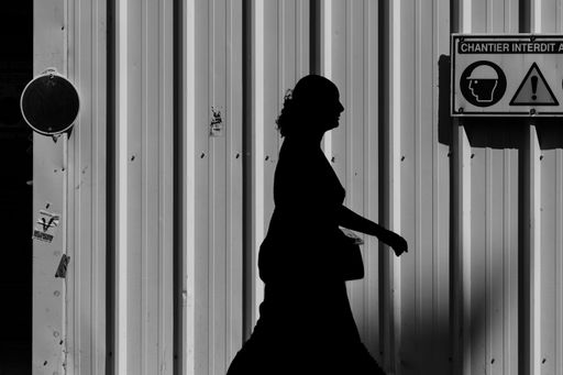 A grayscale silhouette of a walking woman from the side by the building in the daytime