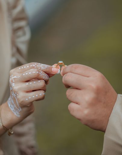 A vertical closeup shot of the couple's hands holding an engagement ring on a blurry background