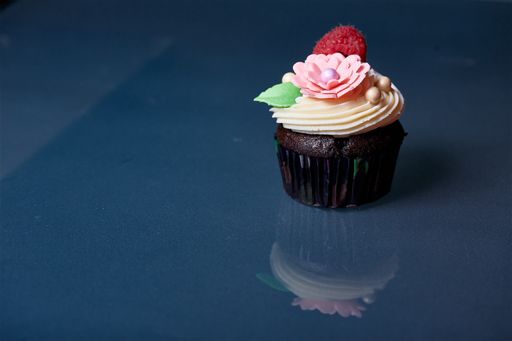 A closeup of a delicious chocolate cupcake, decorated with raspberry and handmade flower and leaf, on a blue surface