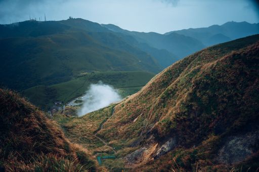 A beautiful shot of orange and green hills and white smoke under a blue sky