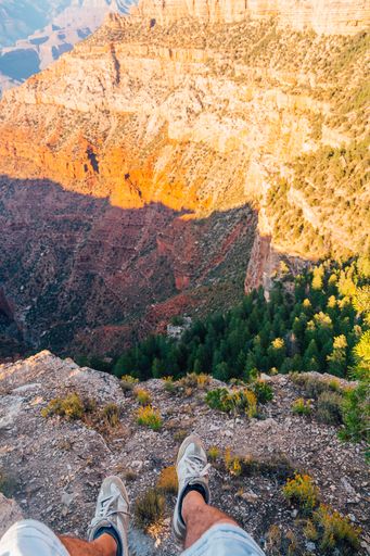 A vertical shot of a young man sitting by the edge of the Grand Canyon exploring the view around him during sunset