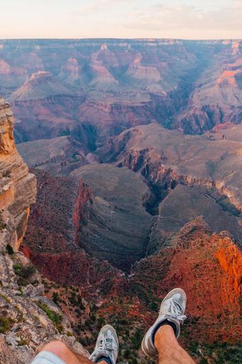 A vertical shot of a young man sitting by the edge of the Grand Canyon exploring the view around him during sunset