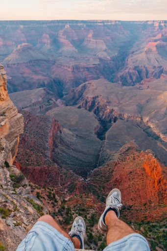 A vertical shot of a young man sitting by the edge of the Grand Canyon exploring the view around him during sunset