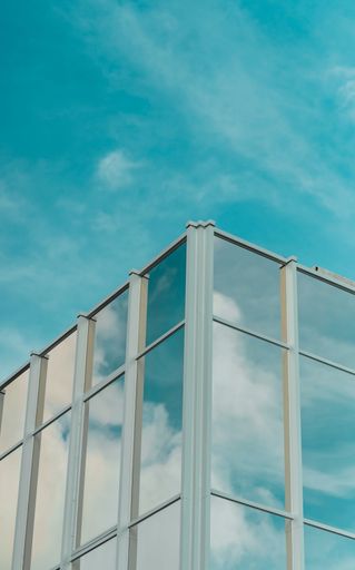 A modern glass-walled building with the reflection of the sky on the surface