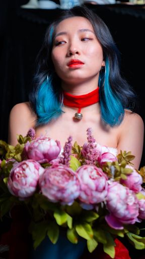 The vertical portrait of an Asian girl with blue-colored hair holding a bucket of roses