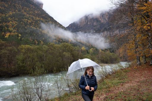 A woman walking with an umbrella with a river and misty mountains in the background