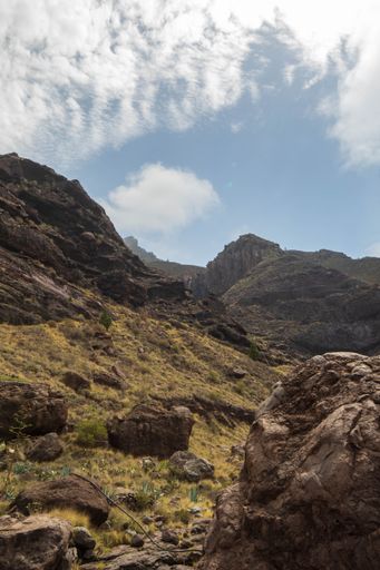 A vertical shot of the rocky slopes under the blue sky with clouds