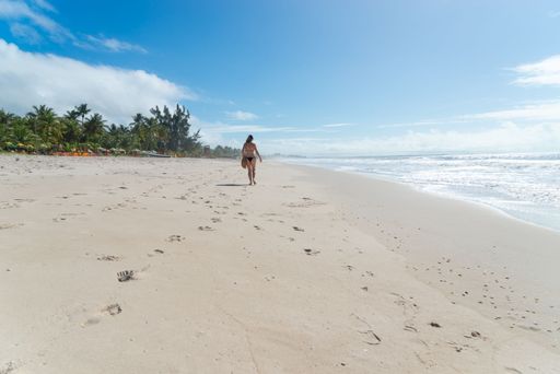 An adult woman in a bikini walking under strong sunlight on Guaibim beach in the city of Valenca, Brazilian state of Bahia. Travel and fun.