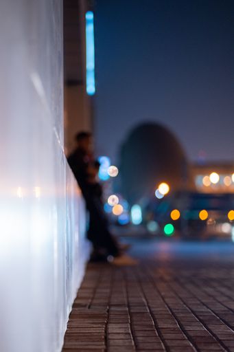 A vertical shot of a white wall and ground with paving slabs at night.