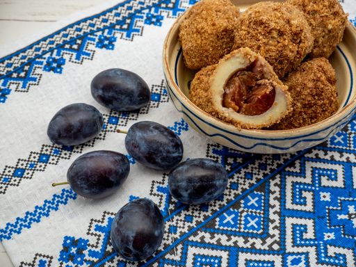 A closeup shot of a plum dumplings bowl on a table with six plum fruits next to it