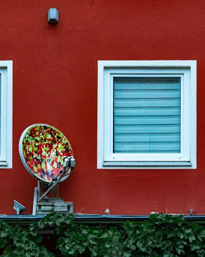 A vertical shot of a pizza satellite dish antenna on a red wall