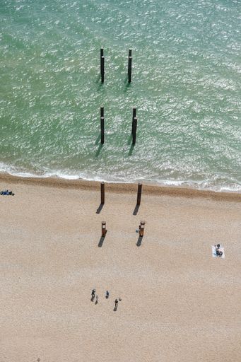 A vertical top view of a sandy beach in front of the clear sea on a sunny day