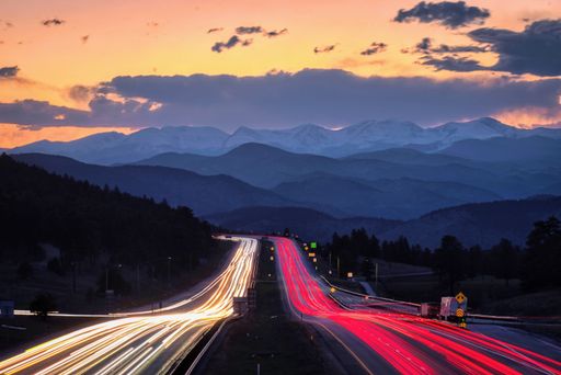 A long-exposure shot of a highway with car lights and a scenic mountainous landscape during sunset