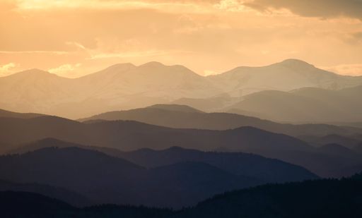 A scenic shot of a mountainous landscape partially covered with fog during the evening golden sunset