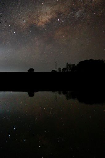 A beautiful scene of silhouette buildings with trees reflecting on lake under starry vista sky