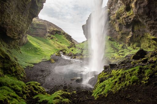 A high-angle closeup of Kvernufoss waterfall with a long exposure effect, cliffs and valleys covered with meadow, cloudy sky background